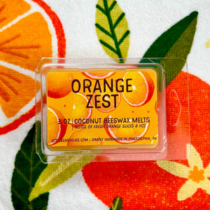 Orange Zest scented wax melt against a background of oranges and leaves