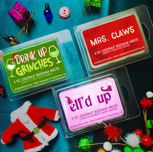 3 oz Drink Up Grinches, Mrs. Claws, and Elf'd Up beeswax and coconut wax melt on blue background with Christmas lights, gift boxes, and a Santa coat. Simply handmade in Philadelphia, PA,