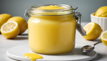 Load image into Gallery viewer, jar of creamy lemon curd on a plate with whole and sliced  lemons in the background
