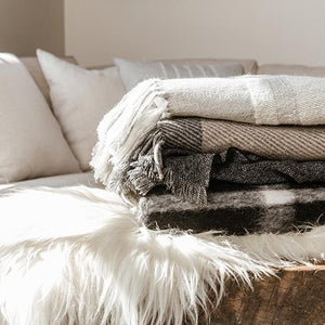 Cashmere Blankets folded on a luxury linen and fur bed with a cedar bed tray wax scent