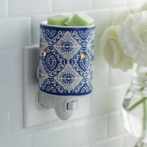 The picture depicts a blue and white wax warmer, a device designed to melt scented wax to release pleasant aromas into the air. The wax warmer has a glossy finish in shades of blue and white. It is compact in size, suitable for plugging into a standard electric outlet, making it convenient to use in various spaces such as bedrooms, living rooms, or offices.