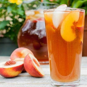 Pint glass with peach iced tea garnished with ice and fresh peaches.