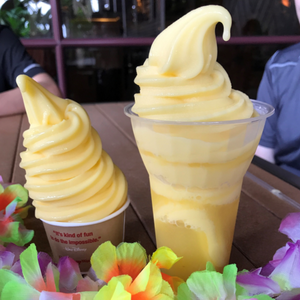Two containers of pineapple whipped ice cream dessert framed by tropical flowers