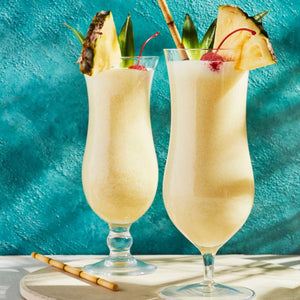 Two tropical Pina colada drinks garnished with pineapple, cherries, and sugar cane sticks